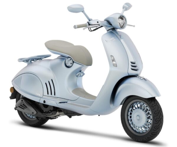 A light blue Vespa scooter with a cream-colored seat, featuring a retro design and sleek lines, parked against a neutral background.