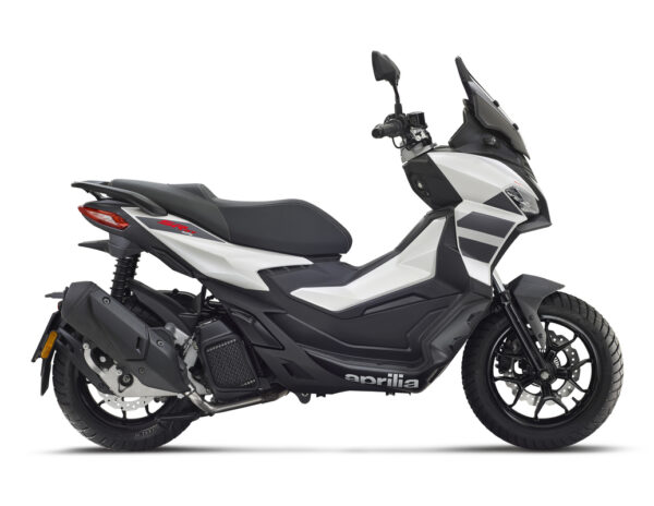 A sleek, modern scooter in white and black, featuring a streamlined design, a tall windshield, and sporty accents, viewed from the side. The scooter displays the brand name "aprilia" prominently on its body.