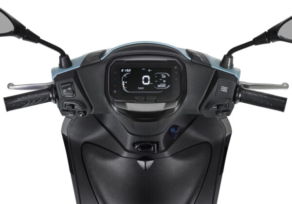 A close-up view of a scooter's handlebars and dashboard, featuring a digital display with trip information and various controls on either side, including switches for lights and an anti-lock braking system.