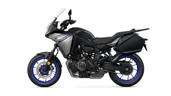 A side view of a modern Yamaha Tracer 9 GT motorcycle, featuring a sleek design with a silver and black color scheme, blue wheels, and a prominent windscreen. The bike is parked against a plain white background.