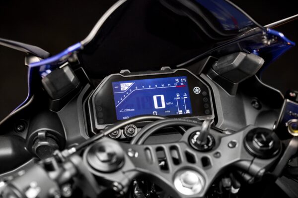 Close-up of a motorcycle dashboard displaying a digital speedometer, gear indicator, and odometer reading, set against a dark background.