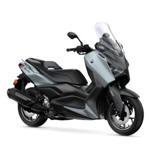 Yamaha 2025 XMAX 300 Tech MAX+ A sleek, modern scooter in a light blue and black color scheme, featuring a tall windshield, comfortable seat, and a sporty design, positioned at an angle to display its profile and wheel.