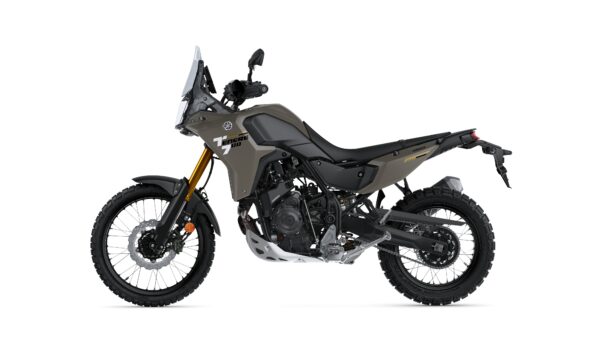 A side view of a Yamaha Tenere 700 adventure motorcycle in a muted green color, featuring knobby tires, a tall windscreen, and a sturdy frame designed for off-road riding.