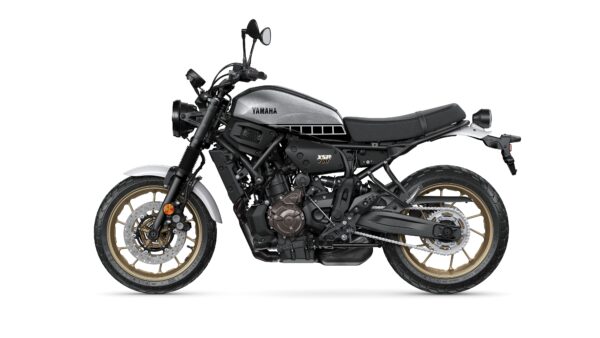 A Yamaha XSR 700 motorcycle is shown in profile, featuring a silver and black design with gold accents on the wheels. The bike has a retro style with a minimalist seat and modern components.