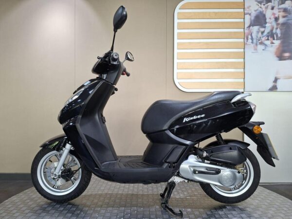A black scooter, model Kisbee, shown from the side against a neutral background with a wooden and photo display. The scooter features a sleek design with a comfortable seat and a visible kickstand.