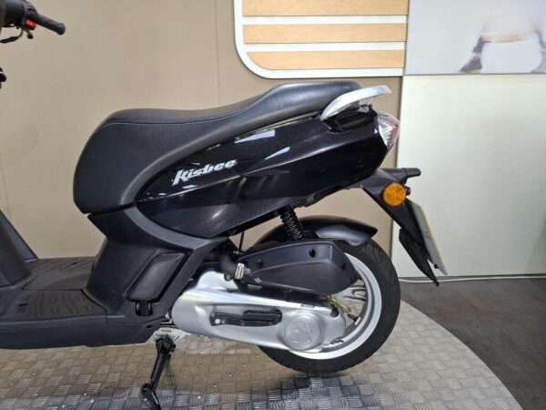 A side view of a black Kisbee scooter, featuring a prominent seat, rear tail light, and tire on a checkered floor.