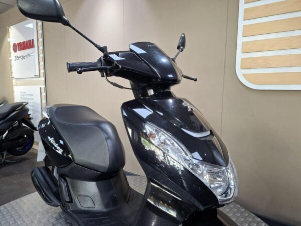 Black scooter parked indoors with polished bodywork and sleek design, featuring a clear windshield and rear-view mirrors.