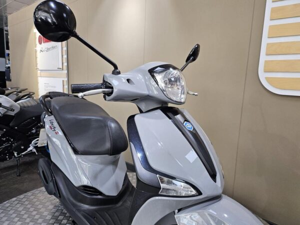 A gray scooter with a black seat and rearview mirrors, showcased against a neutral backdrop. The scooter features a prominent headlight and the model name "Liberty S" visible on the side.