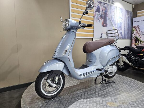 A light blue vintage-style scooter with a brown seat is displayed on a metal platform, set against a modern interior showcasing urban-themed decor.