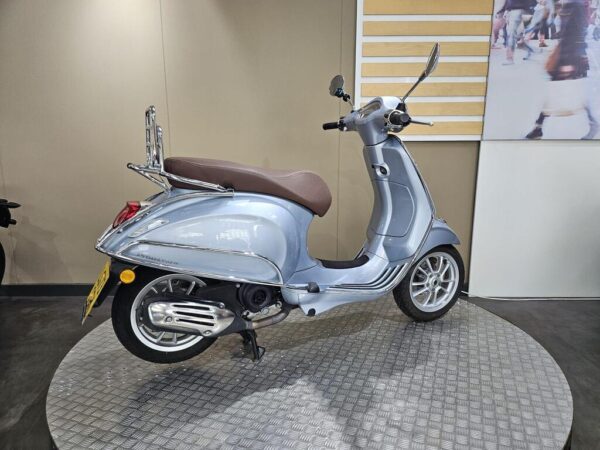 A silver scooter with a brown seat is displayed on a circular platform against a neutral backdrop.