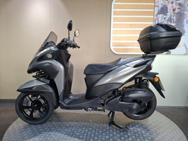 A sleek gray Yamaha scooter displayed in a showroom, featuring a windshield, storage box on the rear, and a modern design.