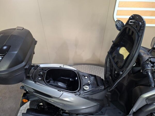 Close-up view of a gray scooter with an open storage compartment and a top case, showcasing its interior design and features against a plain background.