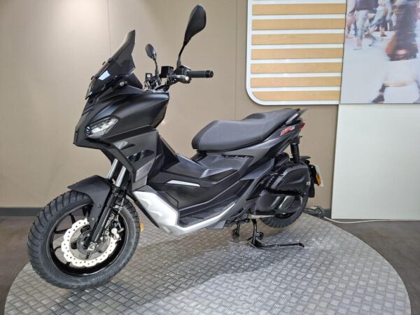 A sleek black scooter with a tall windshield and rugged tires, showcased on a circular platform in a modern setting, featuring a light background.