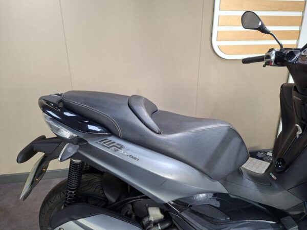 A close-up view of a black scooter seat with a sleek design, set against a neutral background.
