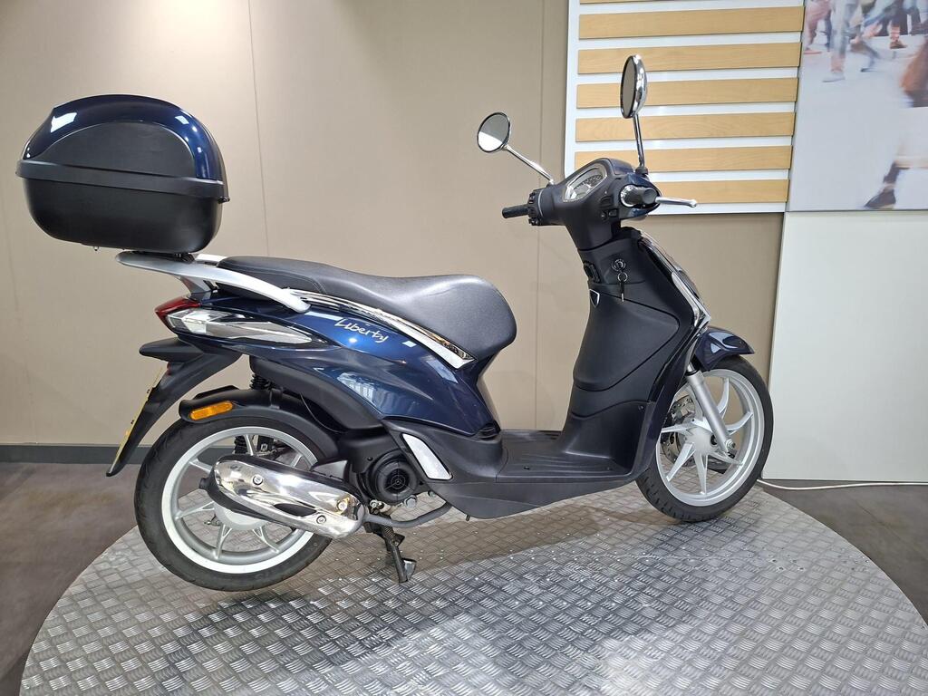 Piaggio Liberty 50 (2019) 10 A dark blue scooter with a sleek design, featuring a black rear trunk, parked on a textured circular platform against a neutral background.