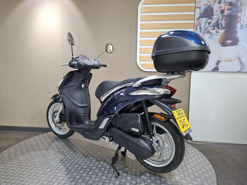 Piaggio Liberty 50 (2019) 14 A dark blue scooter with a black top case is displayed on a circular platform against a neutral background.