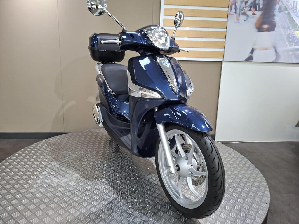 Piaggio Liberty 50 (2019) 21 A blue scooter displayed on a round metallic platform with a neutral-colored background.