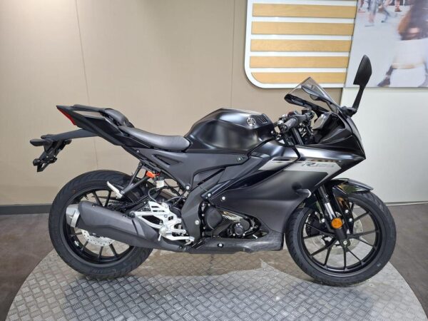 A sleek black Yamaha R15 motorcycle displayed on a textured platform, featuring a modern design with sporty lines and advanced components.