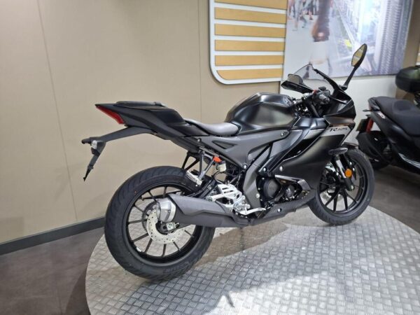 A sleek black motorcycle displayed in a showroom, showcasing its aerodynamic design and modern features, with a partial view of another motorcycle in the background.