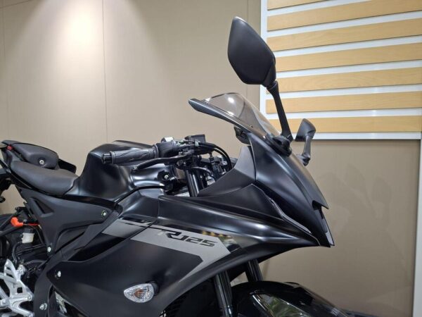 A close-up view of the front section of a black motorcycle, highlighting the handlebars, windshield, and side mirrors against a minimalist background.