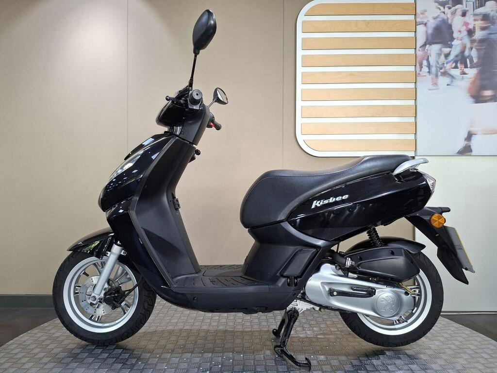 2018 Peugeot Kisbee LC18 NTK 14 A black scooter, model Kisbee, displayed on a textured floor against a neutral wall with a wooden accent and a background image of pedestrians.