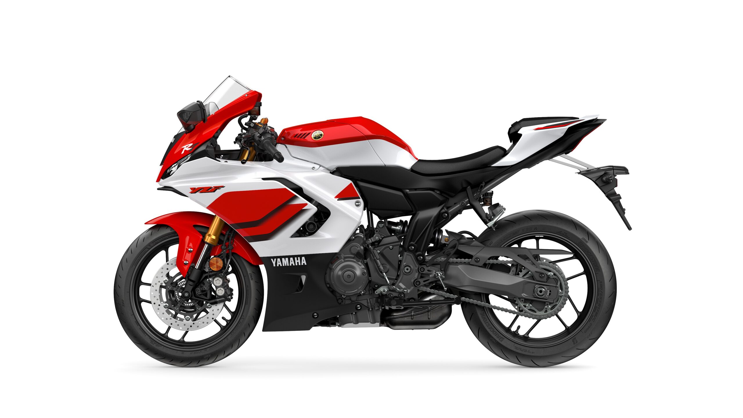 2026 Yamaha R7 Anniversary Edition Left A side view of a red and white Yamaha motorcycle, featuring sleek lines, a sporty design, and a prominent front fairing. The model showcases a modern aesthetic with black accents, a racing-style seat, and high-performance tires.