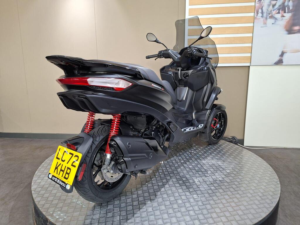 Piaggio MP3 400 LC72 KHB 12 A black scooter with red shock absorbers is displayed on a circular metal platform, showcasing its rear and side profile against a neutral wall background.