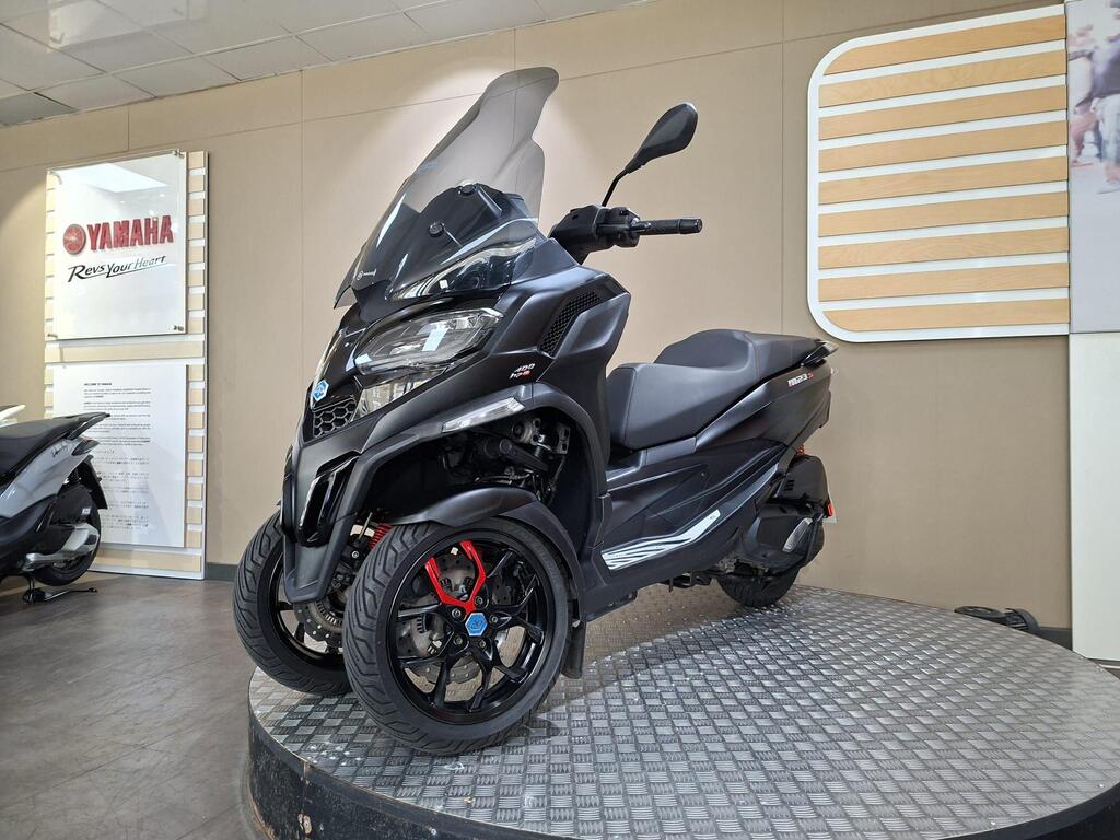 Piaggio MP3 400 LC72 KHB 19 A sleek black three-wheeled scooter showcased on a circular platform in a dealership setting, with a Yamaha logo visible on the wall behind.
