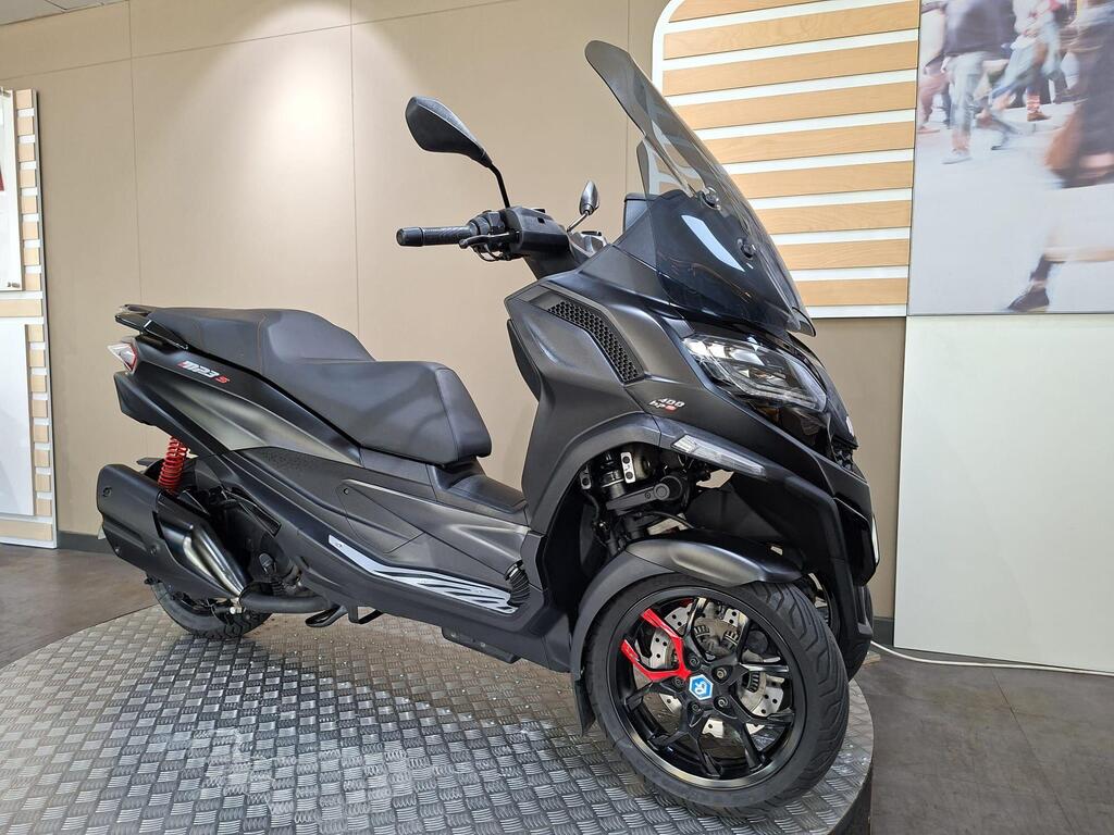 Piaggio MP3 400 LC72 KHB 2 A sleek black scooter with a large windshield, displayed on a circular platform against a minimalist background. The scooter features modern design elements, including a sporty front, red suspension, and stylish wheels.