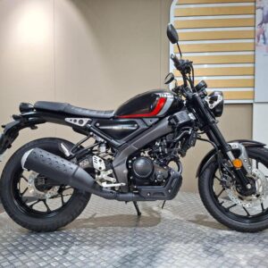 Yamaha XSR125 (2022) A sleek black and red Yamaha motorcycle is displayed on a textured surface in an indoor setting, showcasing its modern design and features.