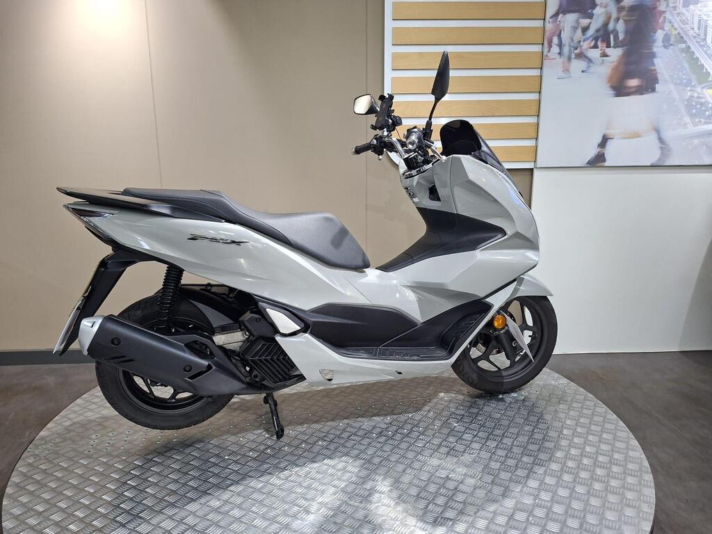 Honda PCX 125 2024 13 A modern silver scooter displayed on a circular, textured platform against a neutral wall backdrop.