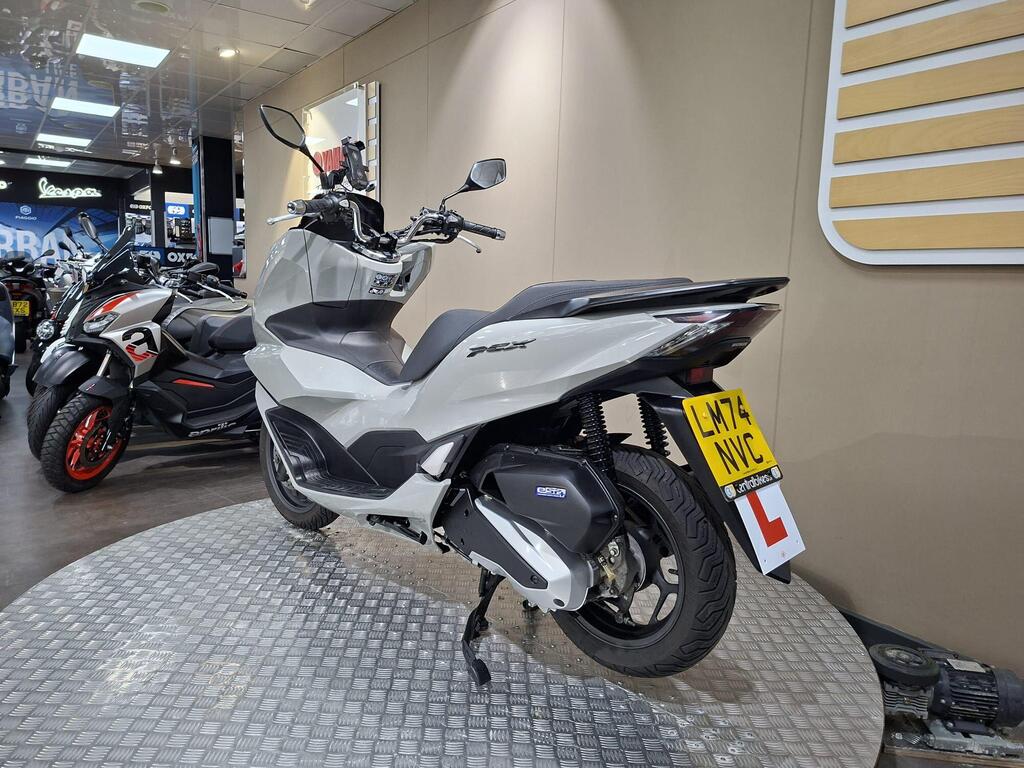 Honda PCX 125 2024 19 A new grey Honda PCX scooter displayed on a rotating stand in a motorcycle showroom, with various other scooters visible in the background.