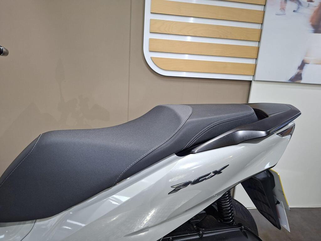 Honda PCX 125 2024 21 A close-up view of the sleek, black seat of a white scooter, featuring a matte finish and modern design, set against a neutral background with wooden paneling.