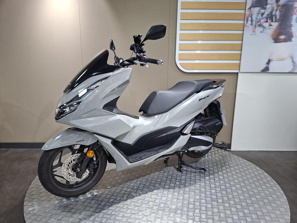 Honda PCX 125 2024 24 A sleek, modern white scooter displayed on a metal platform against a neutral background, showcasing its streamlined design and features.