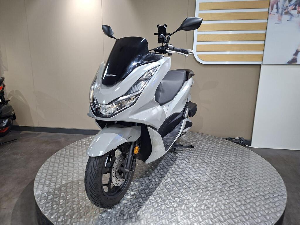 Honda PCX 125 2024 28 A silver Honda scooter displayed on a circular platform, featuring a sleek design and modern details, set against a neutral background.
