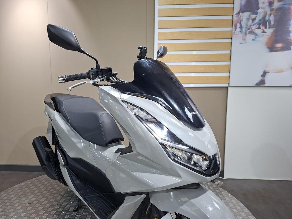Honda PCX 125 2024 29 A close-up view of a gray Honda scooter with a sleek design, featuring a black windshield, a modern headlight, and a minimalist seat, displayed on a circular platform against a neutral background.
