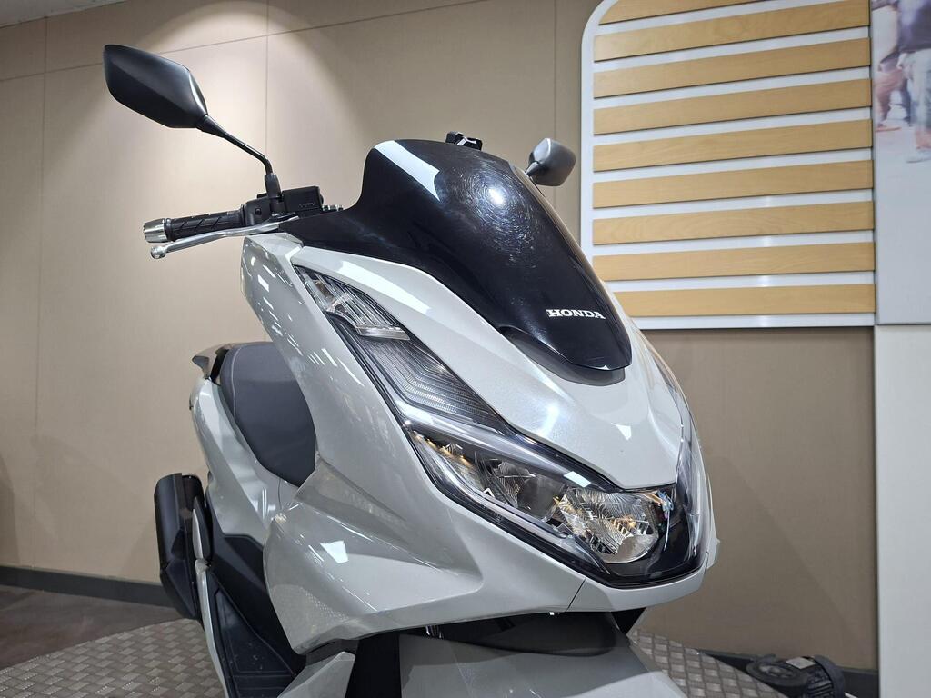 Honda PCX 125 2024 30 A close-up of a white Honda scooter with a sleek design, showcasing its front, headlight, and handlebars against a neutral background.