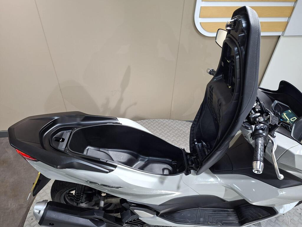 Honda PCX 125 2024 7 A close-up view of a motorcycle seat in an open position, revealing the storage compartment beneath. The bike features a sleek, modern design with a gray body and black accents.