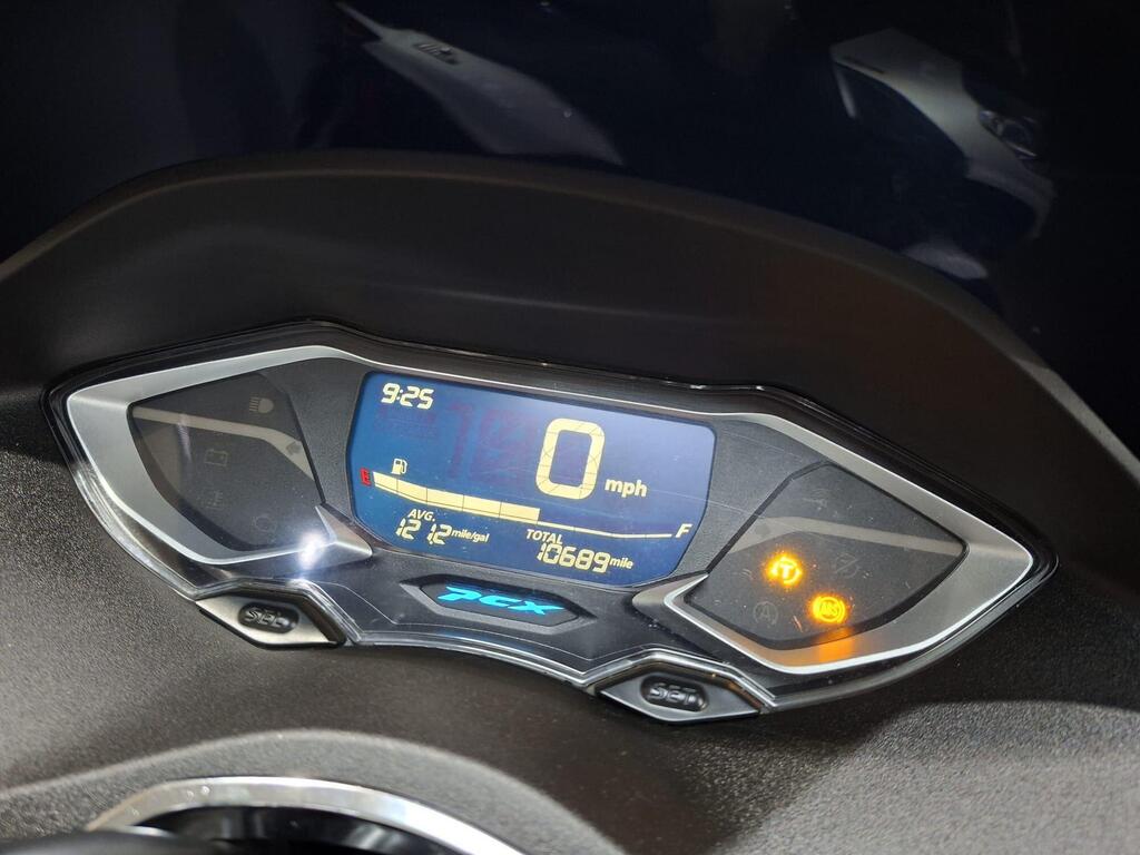 Honda PCX 125 2024 8 Close-up of a motorcycle dashboard display showing the time as 9:25, speed at 0 mph, average mileage of 12 miles per gallon, and total distance of 1069 miles, with warning indicators illuminated.