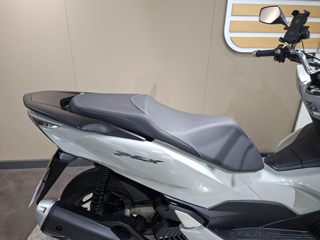 Honda PCX 125 2024 9 A close-up view of a motorcycle seat, showcasing a sleek, modern design in gray and white, with visible suspension components and a minimalist background.