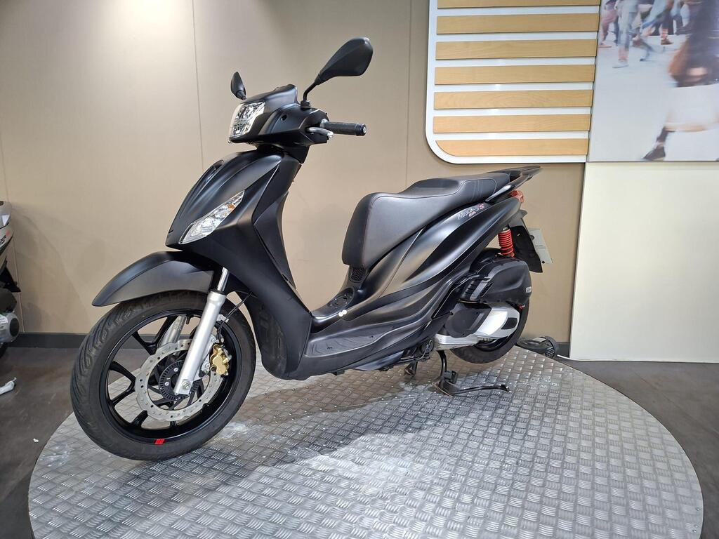 Piaggio Medley (2022) 18 A black scooter displayed on a circular metallic platform against a simple background. The scooter features a sleek design with a prominent front headlight and modern styling.