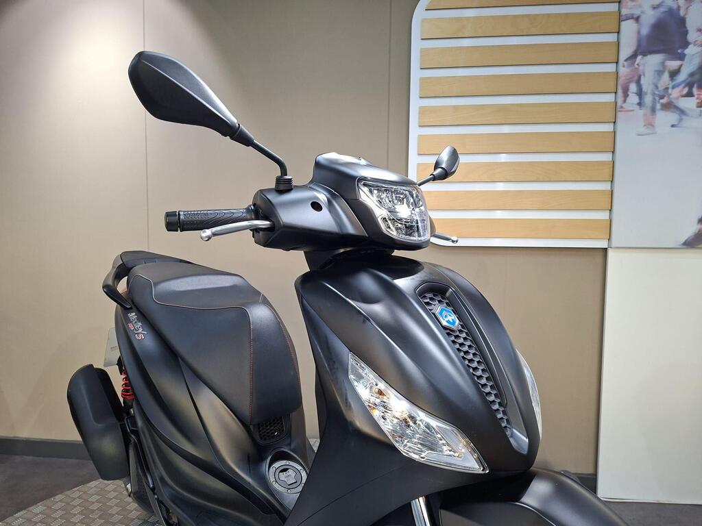 Piaggio Medley (2022) 22 Close-up view of a matte black scooter, highlighting the handlebars, mirrors, and front headlight, against a neutral background with subtle textures.