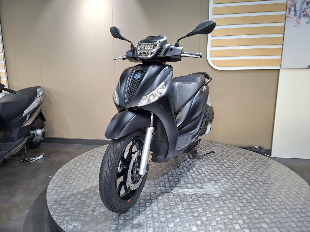Piaggio Medley (2022) 23 A sleek black scooter showcased on a circular platform, highlighting its modern design and features, set against a neutral wall background.