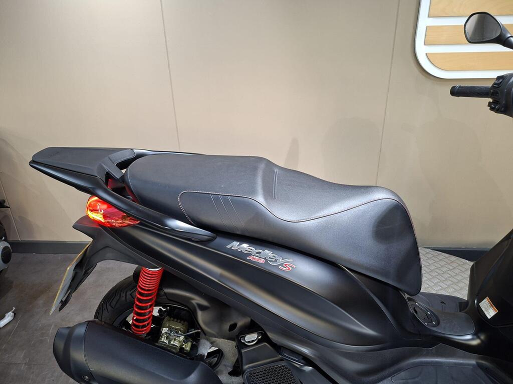 Piaggio Medley (2022) 5 A close-up view of the black seat of a motorcycle, featuring stylish stitching and a sleek design, with a red shock absorber visible beneath.