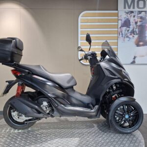 Piaggio MP3 300 HPE Sport (2019) A black three-wheeled scooter with a rear storage box, displayed against a neutral background featuring a graphic with pedestrians and a modern cityscape.