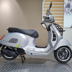 Vespa GTS 125 Supertech (2023) A silver scooter displayed on a circular platform against a neutral backdrop, featuring a sleek design and modern details.