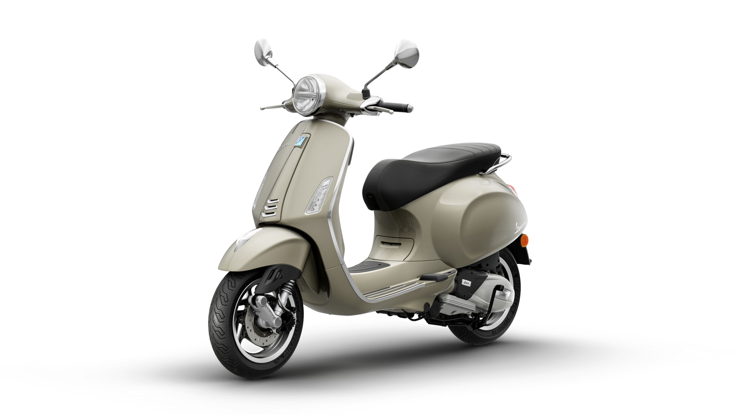 Primavera 125 2026 Beige Avvolgente Lateral Left A beige scooter with a retro design, featuring a round headlight, chrome mirrors, and a plush black seat, positioned at a slight angle against a white background.