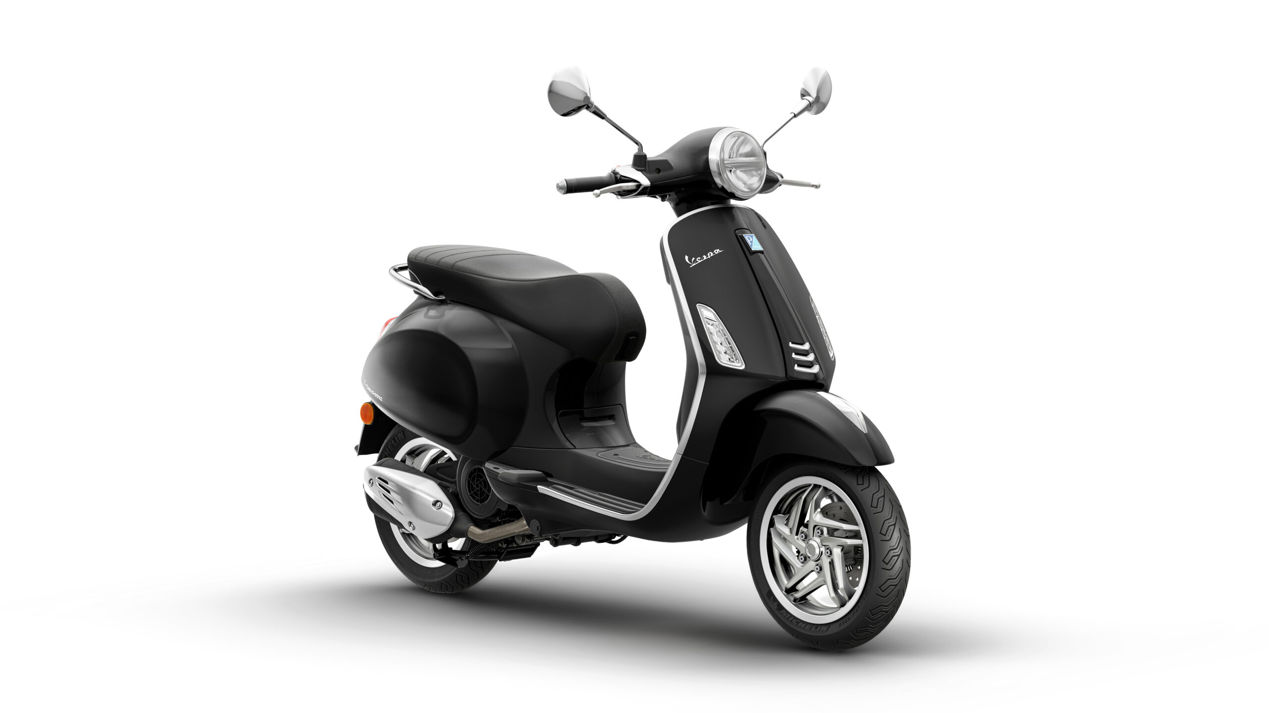 Primavera 125 2026 Nero Convinto Lateral Right A black Vespa scooter is positioned at a slight angle, showcasing its sleek design, chrome accents, and comfortable seating. The scooter has a round headlight, mirrors, and a silver exhaust pipe, with a clean white background.
