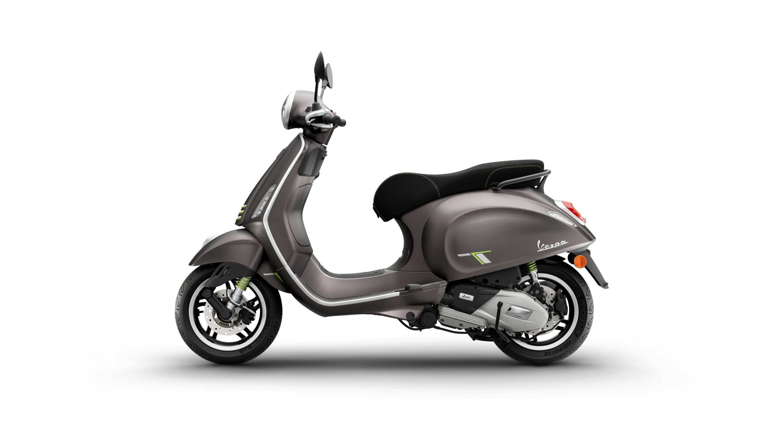 Primavera Tech 125 2026 Grigio Ottimista Left A modern gray Vespa scooter is shown from the side, featuring a sleek design, black seat with green accents, and a silver exhaust. The background is plain white.