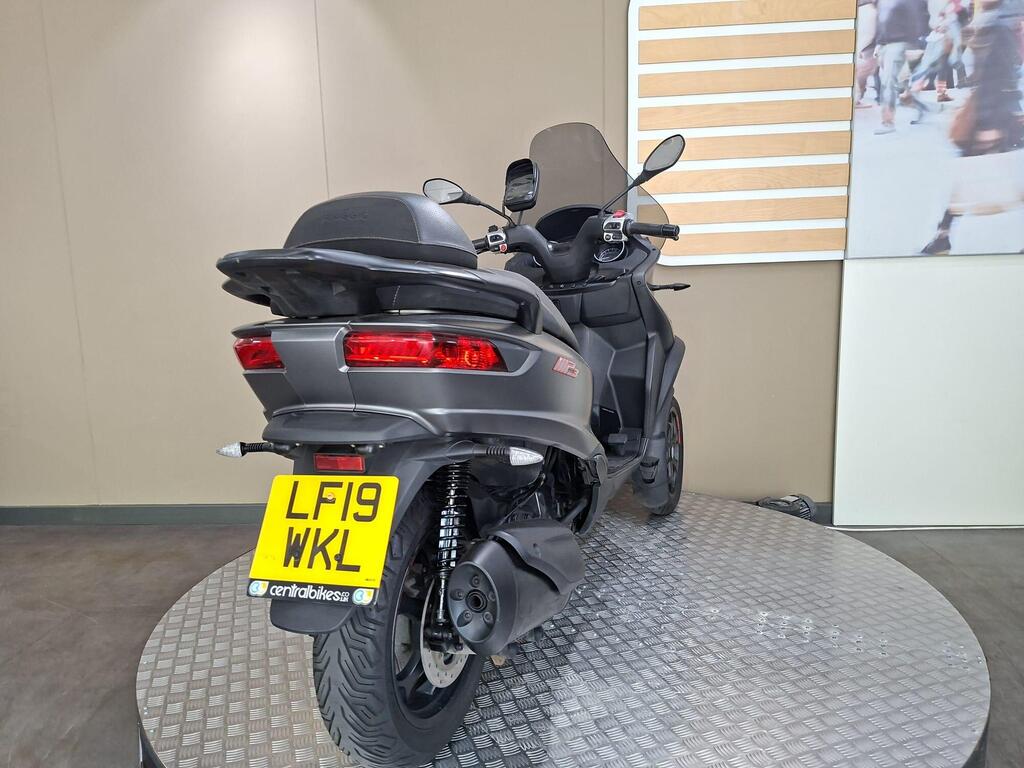 Piaggio MP3 350 2019 14 A black three-wheeled scooter with a prominent rear view, featuring a license plate that reads "LF19 WKL." It is displayed on a circular, textured platform with a neutral background.